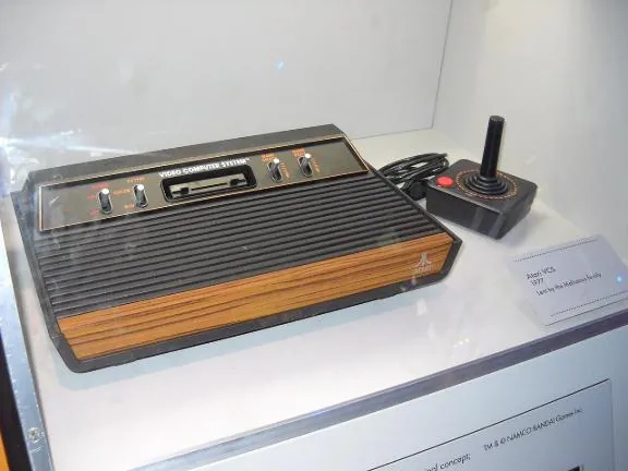A woodgrain Atari VCS console and joystick in a museum case beside its label