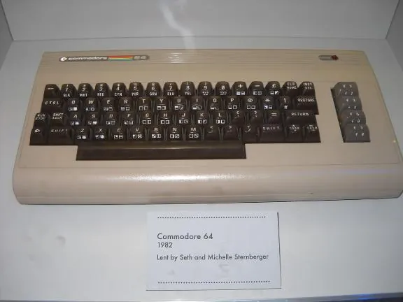 A Commodore 64 computer in a museum case beside its label
