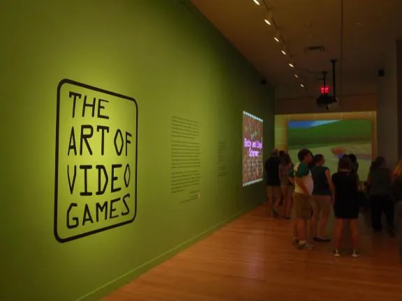 The exhibition title wall, painted green, with visitors walking into the first gallery