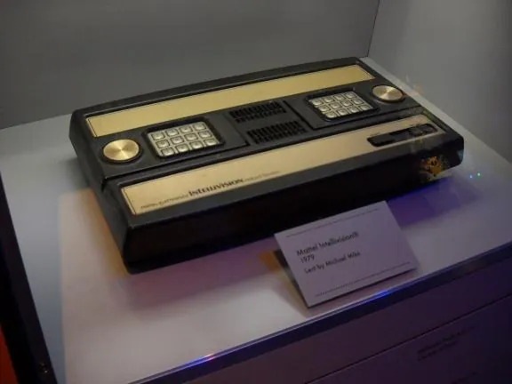 A Mattel Intellivision console with gold trim in a museum case