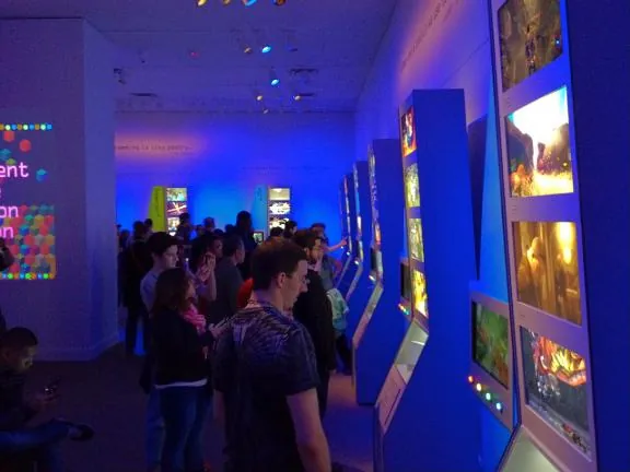 Visitors lined up along a row of blue-lit kiosks showing game screens