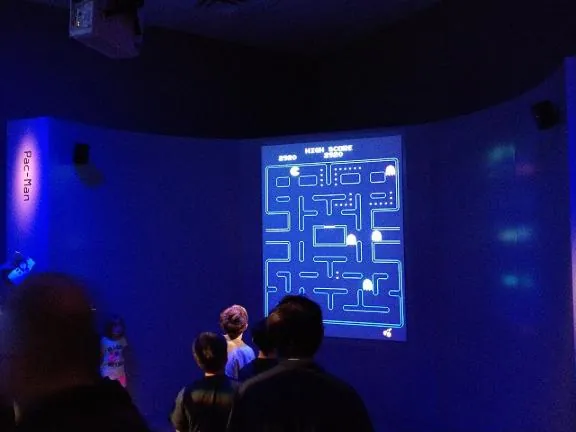 Visitors watching Pac-Man projected on a tall screen in a darkened room