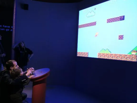 An adult and a child playing Super Mario Brothers on a wall-sized projection