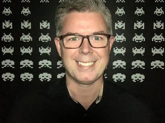 Chris Melissinos smiling in front of a wall of pixel-art alien invaders